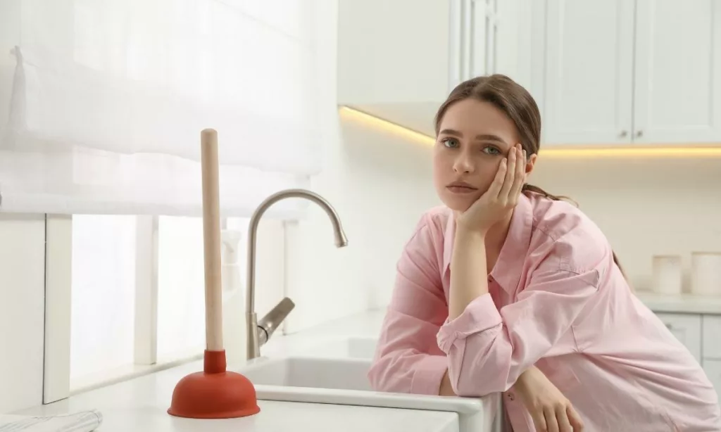 Woman leaning on the counter by the sink with a plunger on it