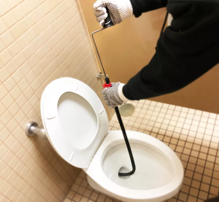 Man using a toilet Auger in a restroom